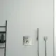 Ideal Standard Thermostat mit einem Bedienfeld und zwei Auslässen, montiert an einer hellen Wand. Ein Regal mit Pflegeprodukten ist auf der linken Seite sichtbar.